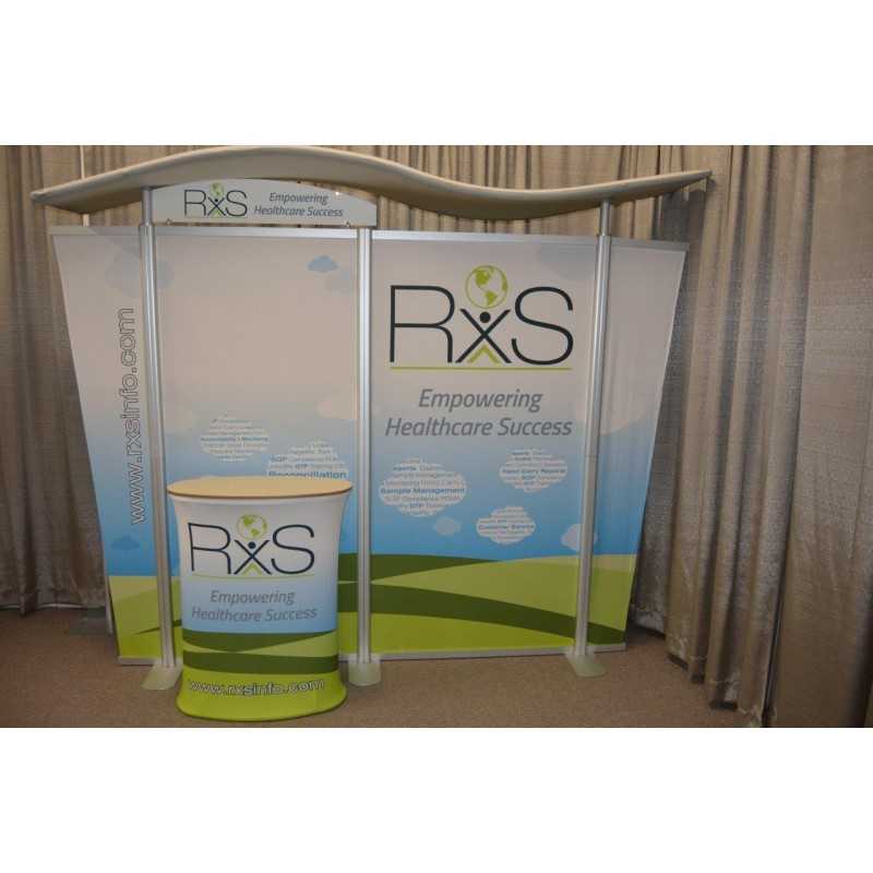 The 10ft Timberline Wave Canopy Tapered Kit 5 by Affordable Exhibit Displays showcases the RxS logo and 'Empowering Healthcare Success' on a green, blue, and white SEG fabric backdrop and podium featuring a stylized person with leaf.