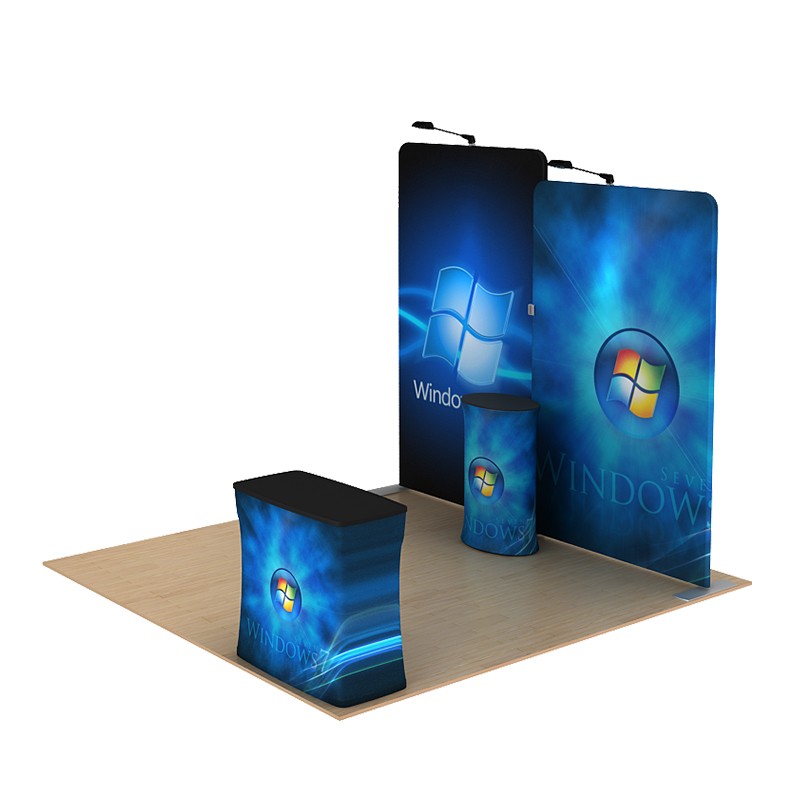 A 10ft Waveline Media B-Series Scallop Kit B by Affordable Exhibit Displays features Windows branding with blue graphics, the Windows logo, and text on display walls, a counter, and a pedestal set on a light wood floor.