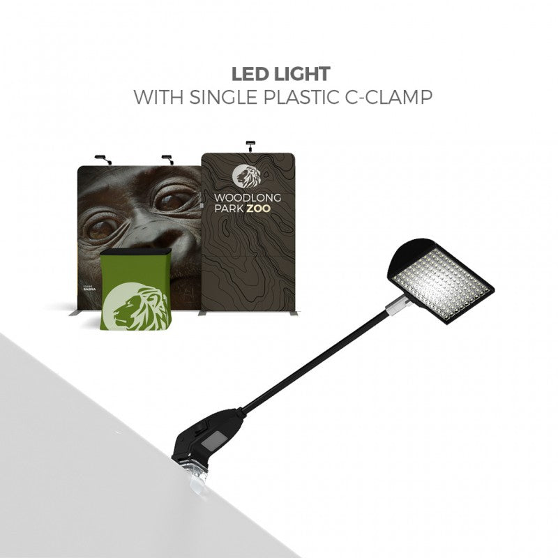 LED light with a single plastic C-clamp attached to a surface, shown in front of a Woodlong Park Zoo booth featuring animal graphics, a gorilla close-up, and the 20ft Waveline Media M-Series Kit 06 by Affordable Exhibit Displays.