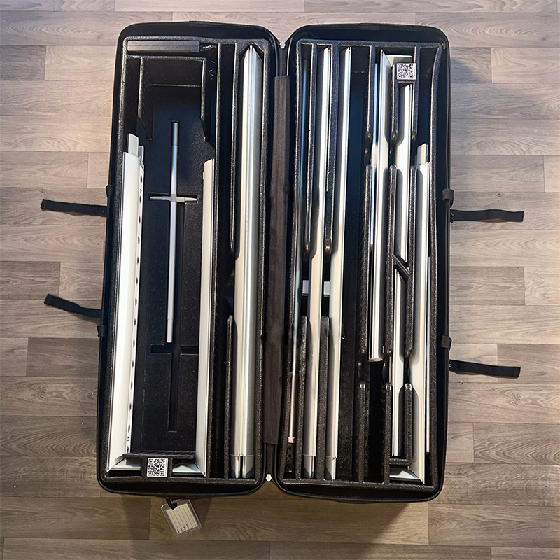 The 20ft BrightLine MKKM Kit by Affordable Exhibit Displays is shown in an open black hard case with custom foam compartments holding neatly arranged metal rods and parts, ideal for SEG trade show displays. The case rests on a light wood floor.