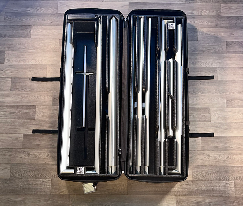 A 20ft BrightLine JNNJ Kit by Affordable Exhibit Displays is open on a wooden floor, displaying neatly organized silver and black components inside custom foam compartments—ideal for SEG backlit trade show display graphics.
